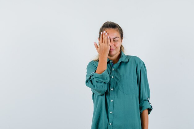 Mujer joven sosteniendo la mano en su rostro con camisa azul y mirando en secreto