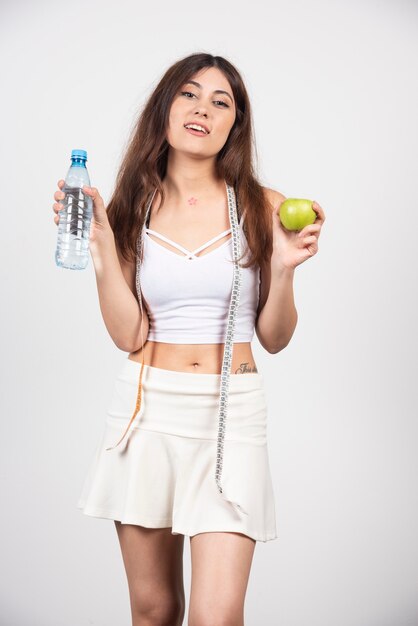 Mujer joven sosteniendo una manzana y una botella de agua.