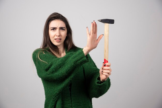 Mujer joven sosteniendo un martillo en las manos sobre un fondo gris.