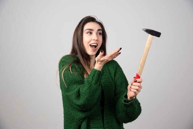 Mujer joven sosteniendo un martillo en las manos sobre un fondo gris.