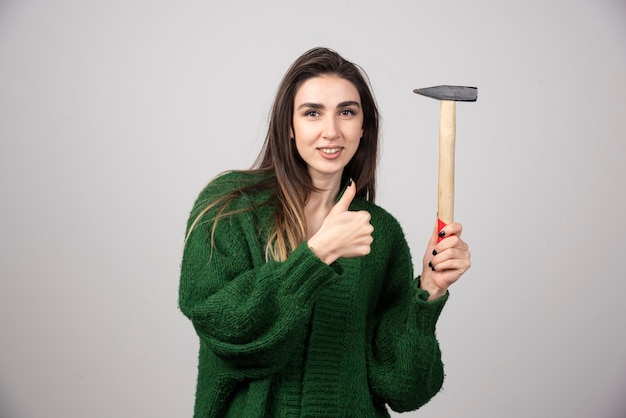 Foto gratuita una mujer joven sosteniendo un martillo y mostrando un pulgar hacia arriba.