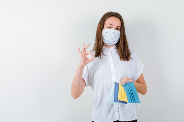 Mujer joven sosteniendo máscaras médicas y mostrando el signo de ok