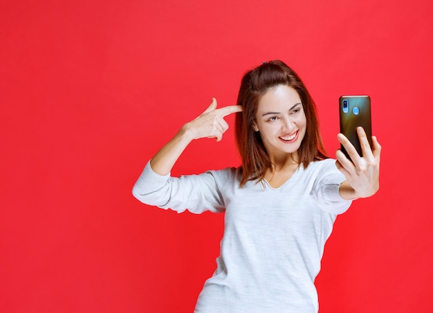 Mujer joven sosteniendo un nuevo modelo de teléfono inteligente negro y haciendo una videollamada o tomando su selfie