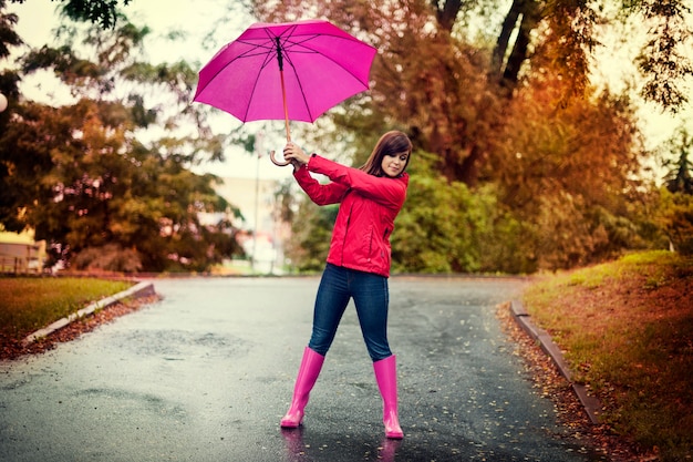 Mujer joven sosteniendo paraguas rosa en un parque