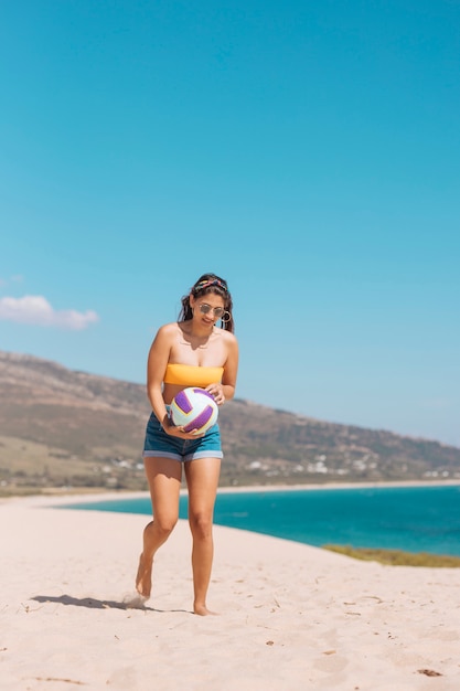 Mujer joven sosteniendo la pelota por la orilla del mar