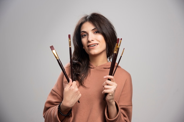 Mujer joven sosteniendo pinceles en gris