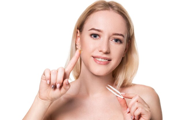 Mujer joven sosteniendo pinzas para lentes de contacto y lentes frente a su cara sobre fondo blanco. Concepto de vista y oftalmología.