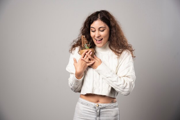 Mujer joven sosteniendo una planta con expresión feliz. Foto de alta calidad