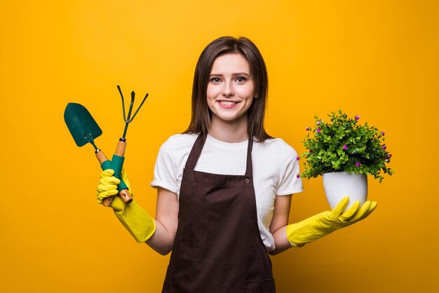 Mujer joven sosteniendo una planta y herramientas aisladas