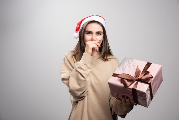 Mujer joven sosteniendo un regalo de Navidad sobre un fondo gris.