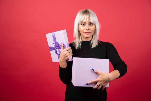 Mujer joven sosteniendo un regalo en una pared roja.