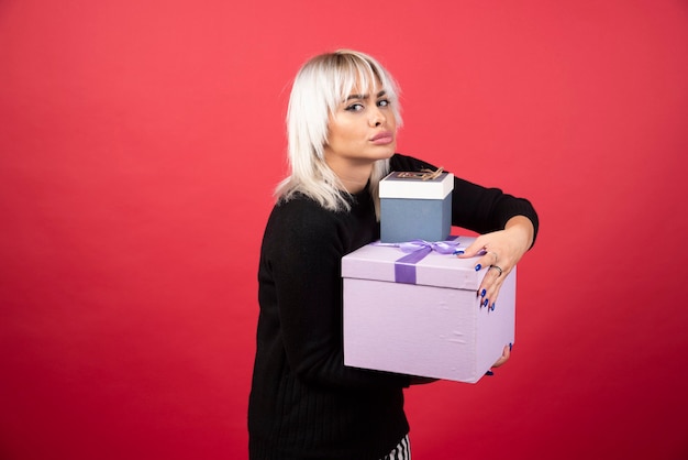 Mujer joven sosteniendo regalos en una pared roja.