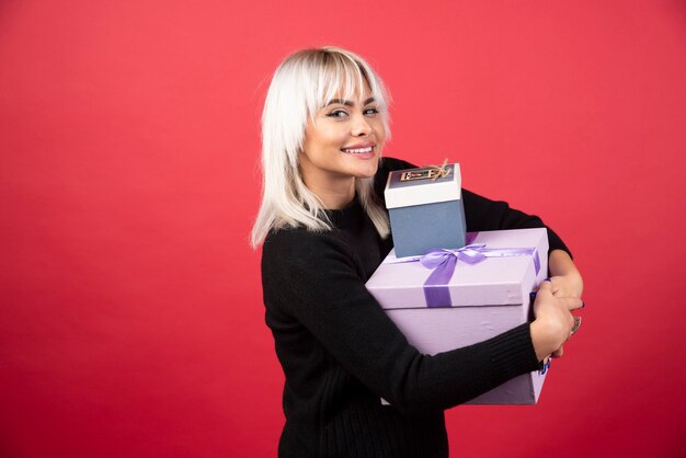 Mujer joven sosteniendo regalos en una pared roja.