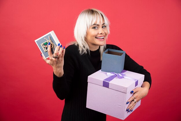 Mujer joven sosteniendo regalos en una pared roja.