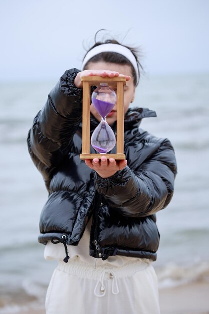 Mujer joven sosteniendo un reloj de arena en la playa Foto de alta calidad