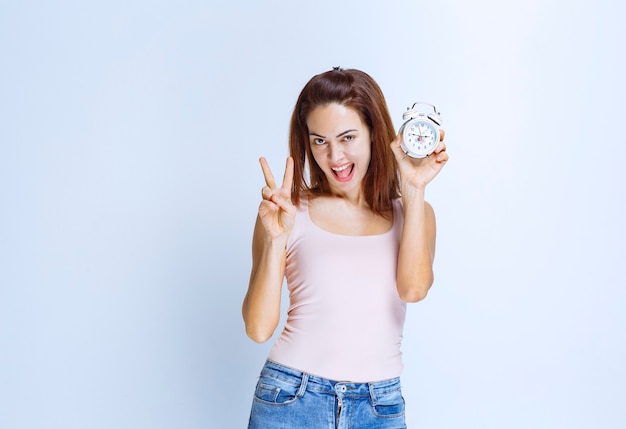 Mujer joven sosteniendo un reloj despertador y apuntando a él