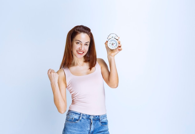 Mujer joven sosteniendo un reloj despertador y sintiéndose exitoso