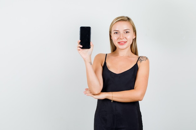 Mujer joven sosteniendo smartphone en camiseta negra y mirando alegre