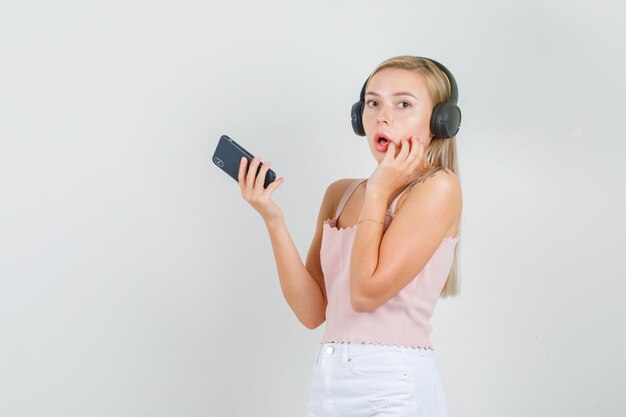 Mujer joven sosteniendo smartphone con la mano en la cara en camiseta