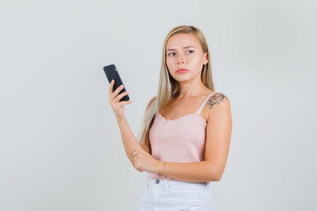 Mujer joven sosteniendo smartphone mientras mira a un lado en camiseta