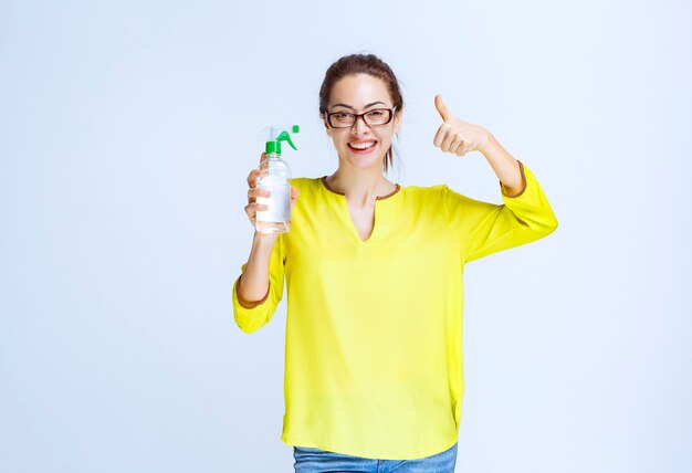 Mujer joven sosteniendo un spray de limpieza y mostrando signo de disfrute