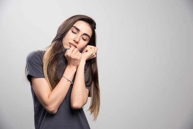 Mujer joven sosteniendo su camiseta sobre un fondo gris