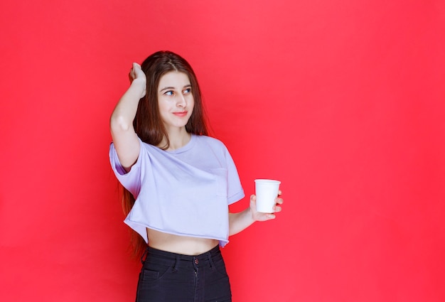 mujer joven sosteniendo una taza de agua desechable blanca y pensando.