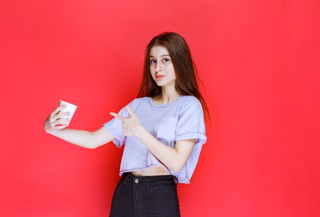 mujer joven sosteniendo una taza de agua desechable blanca.