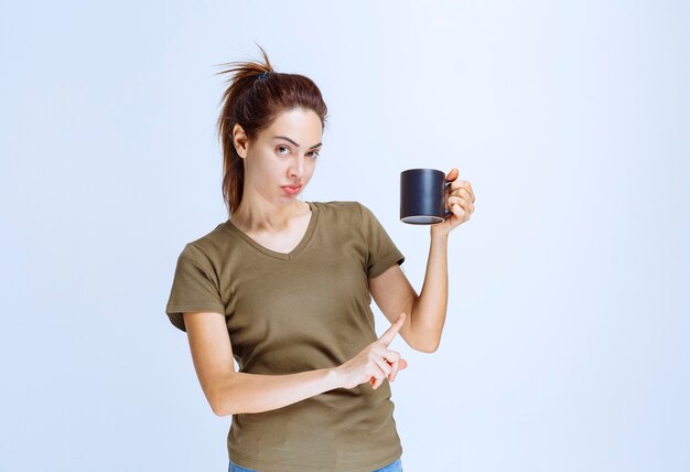 Mujer joven sosteniendo una taza de bebida y apuntando a ella