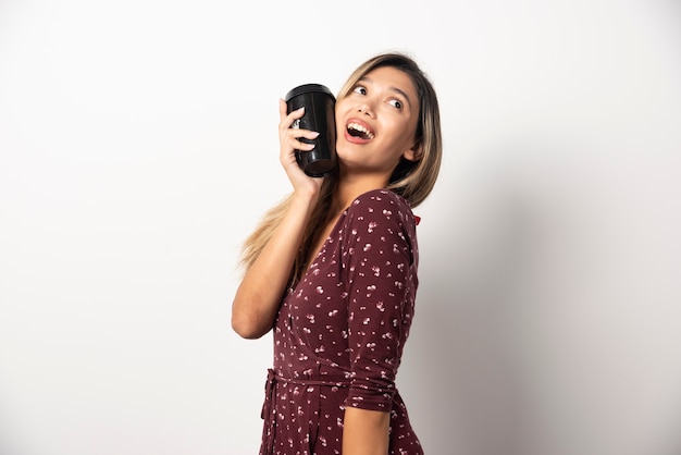 Mujer joven sosteniendo una taza de bebida en la pared blanca.