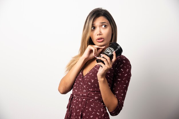 Mujer joven sosteniendo una taza de bebida en la pared blanca.