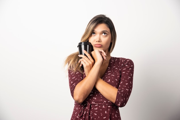 Mujer joven sosteniendo una taza de bebida en la pared blanca.