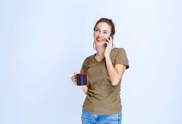 Mujer joven sosteniendo una taza de café y hablando por teléfono