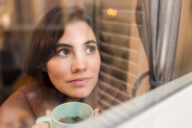 Mujer joven sosteniendo una taza de café mientras está cubierto con una manta