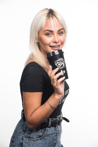 Mujer joven sosteniendo una taza de café en la pared blanca con expresión feliz.