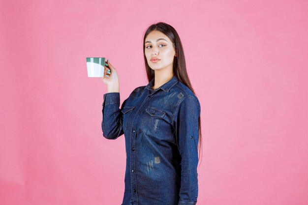 Mujer joven sosteniendo una taza de café verde blanco y oliendo