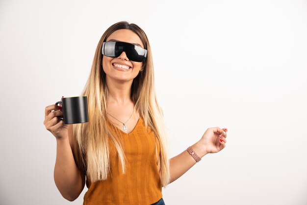 Mujer joven sosteniendo taza negra y gafas protectoras.