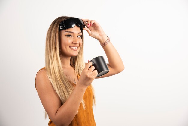 Mujer joven sosteniendo taza negra y gafas protectoras.