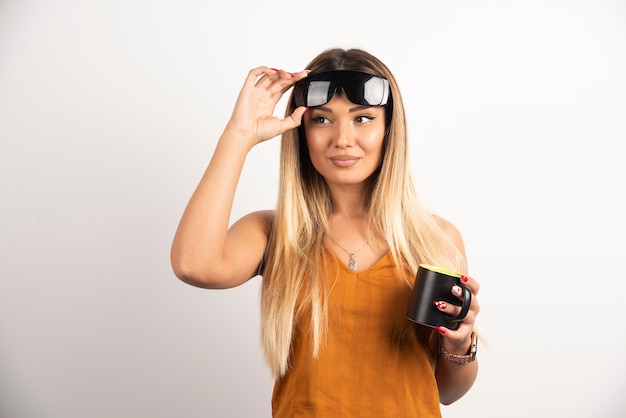 Mujer joven sosteniendo taza negra y gafas protectoras.