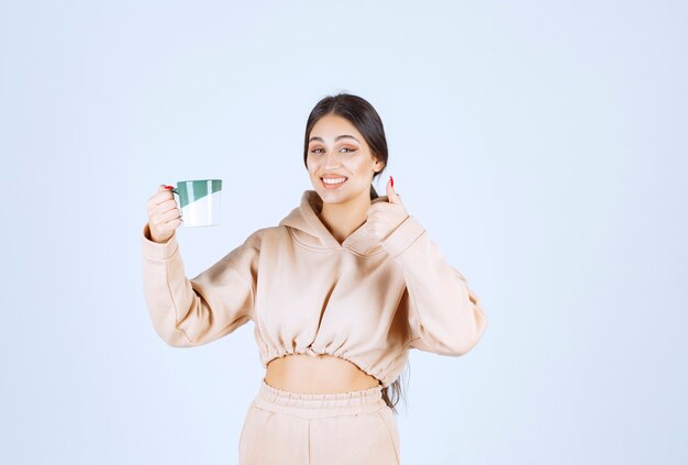 Mujer joven sosteniendo una taza verde y mostrando su satisfacción