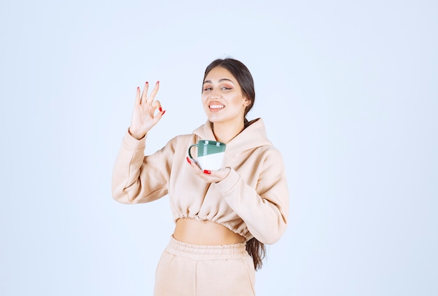 Mujer joven sosteniendo una taza verde y mostrando su satisfacción