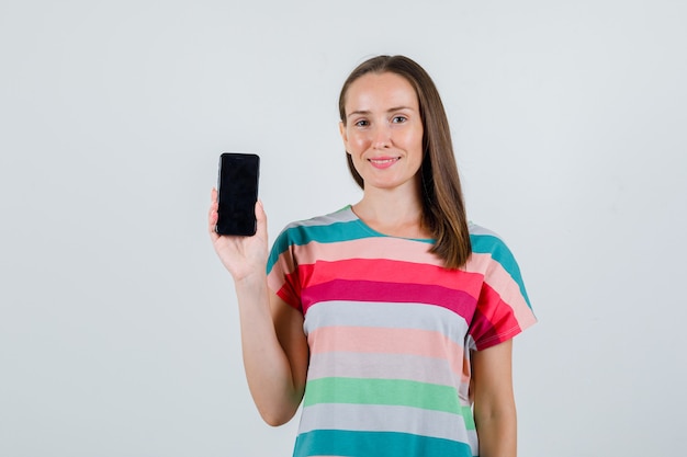 Mujer joven sosteniendo teléfono móvil en camiseta y mirando alegre. vista frontal.