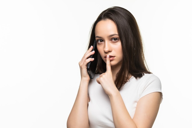 Mujer joven sosteniendo teléfono móvil y mostrando gesto de silencio aislado en un gris