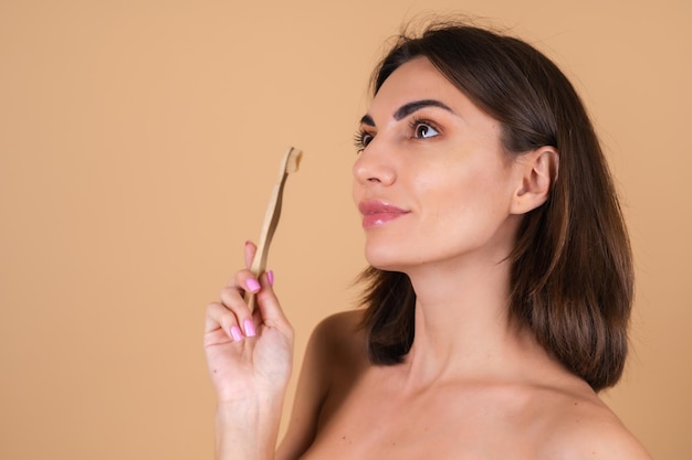 Mujer joven sostiene un cepillo de dientes de madera ecológico, cuidando la naturaleza y los dientes