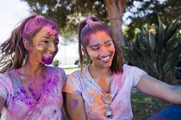 Mujer joven con su amiga cubierta de polvo holi tomando selfie en móvil