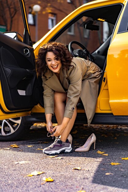 mujer joven en su auto, un mundo de mujeres fuertes y exitosas. La mujer al volante se cambia de ropa, los zapatos en tacones de aguja se cambian por zapatillas