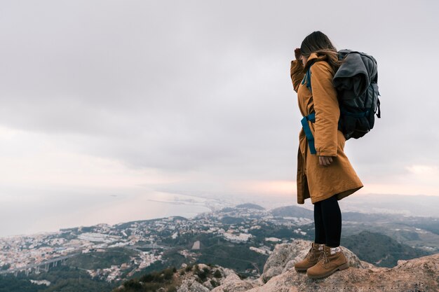 Mujer joven con su mochila de pie en la cima de la montaña mirando la vista idílica