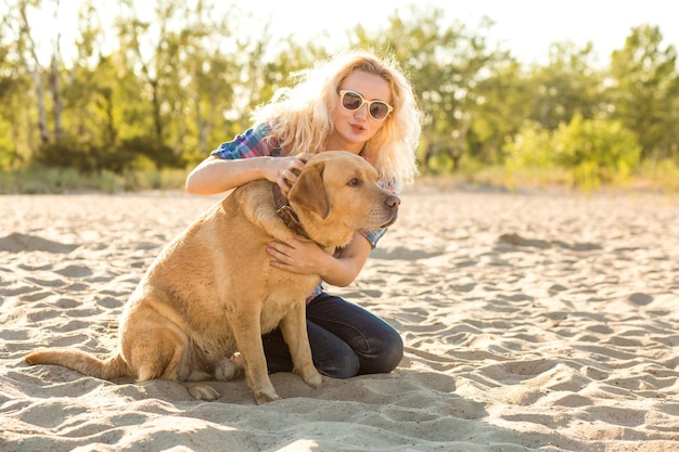 Mujer joven con su perro en la playa. Una mujer joven se sienta en la arena con su perro. Labrador