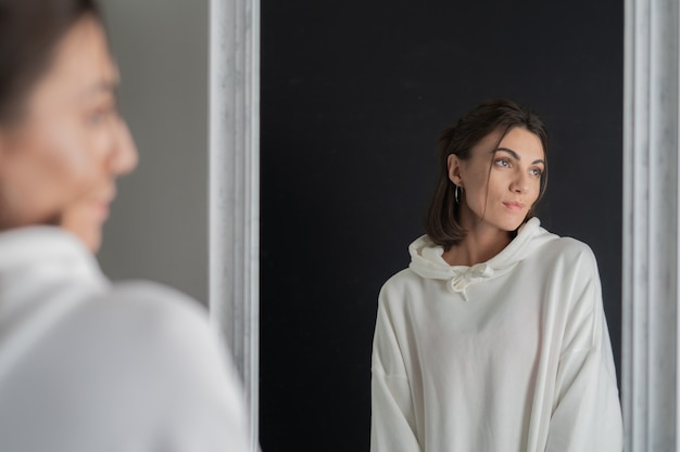 Foto gratuita mujer joven en sudadera con capucha blanca posando en el espejo