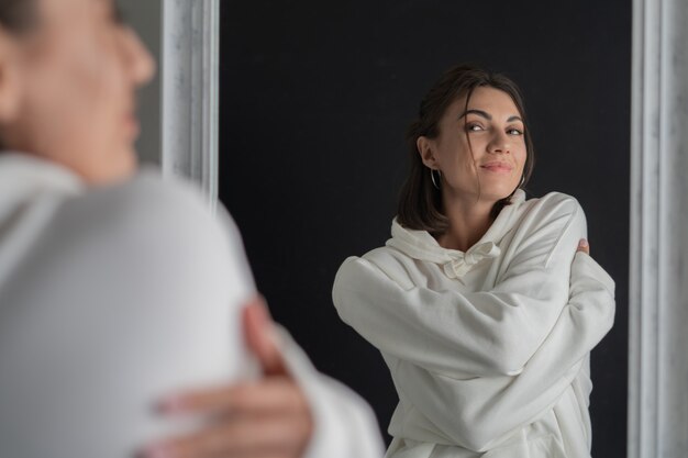 Mujer joven en sudadera con capucha blanca posando en el espejo